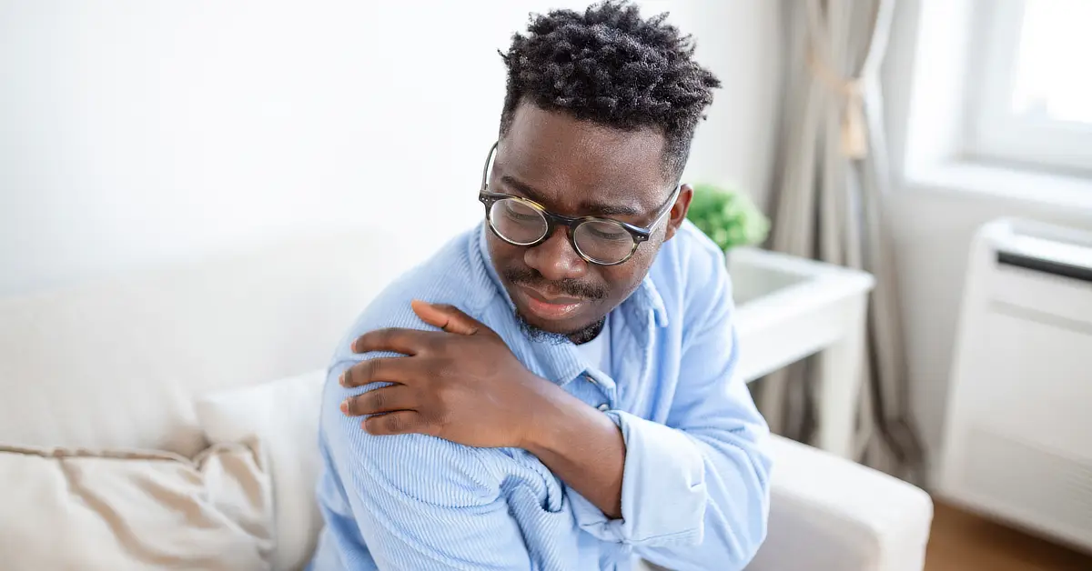 black man holding right shoulder in pain.